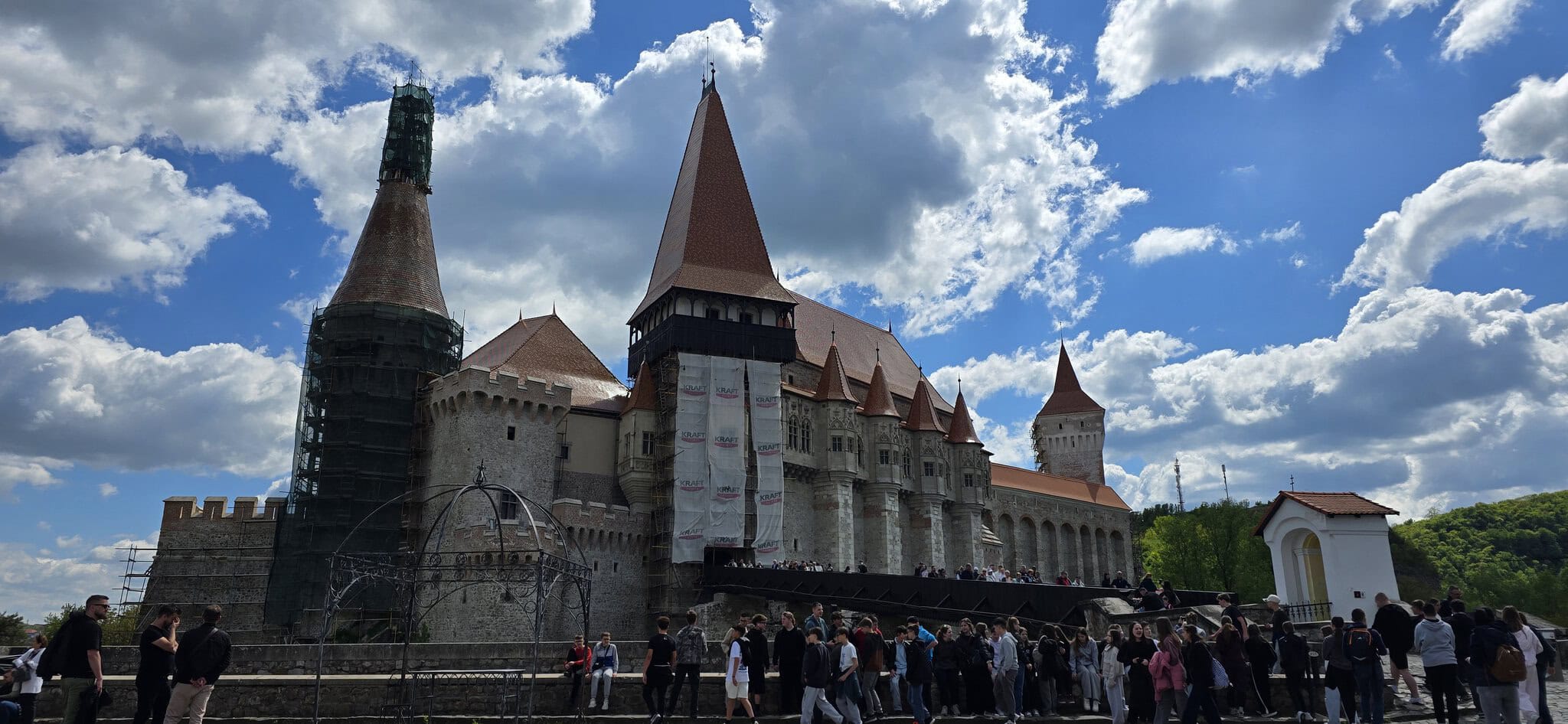 Turnul Castelului medieval cu acoperișuri ascuțite și ziduri de piatră, sub cerul înnorat, cu mulțim.