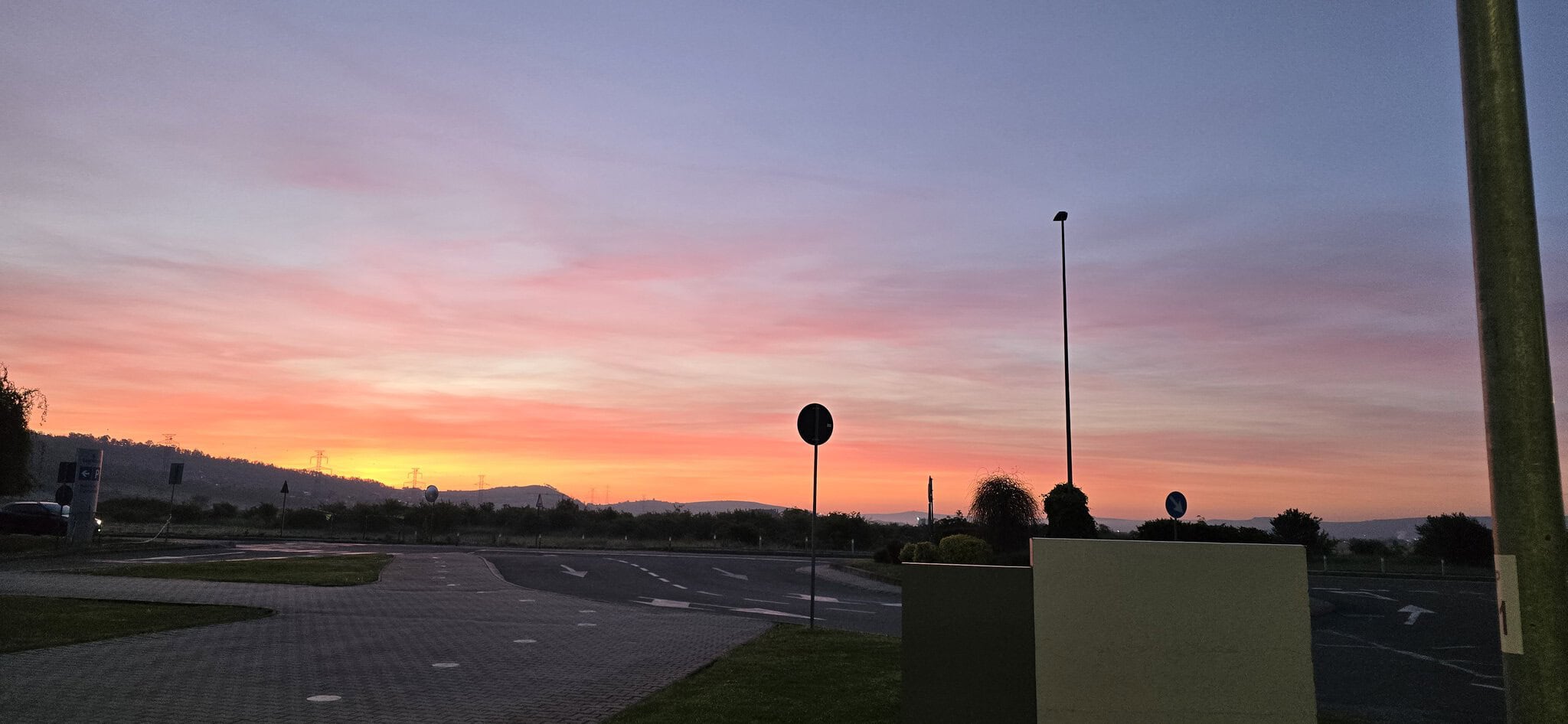 Vedere de apus de soare peste o zonă urbană cu semne de circulație și un cer colorat în nuanțe de ro.