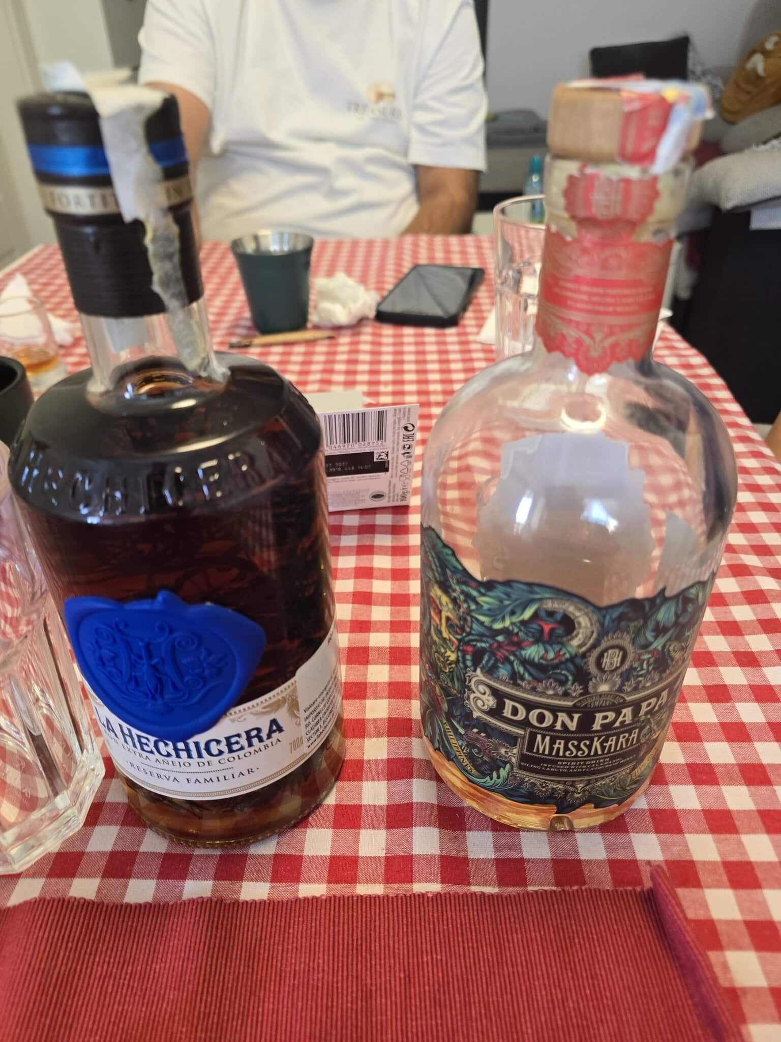 Două sticle de rom premium, La Hechicera și Don Papa Masskara, așezate pe o față de masă în carouri roșii și albe.